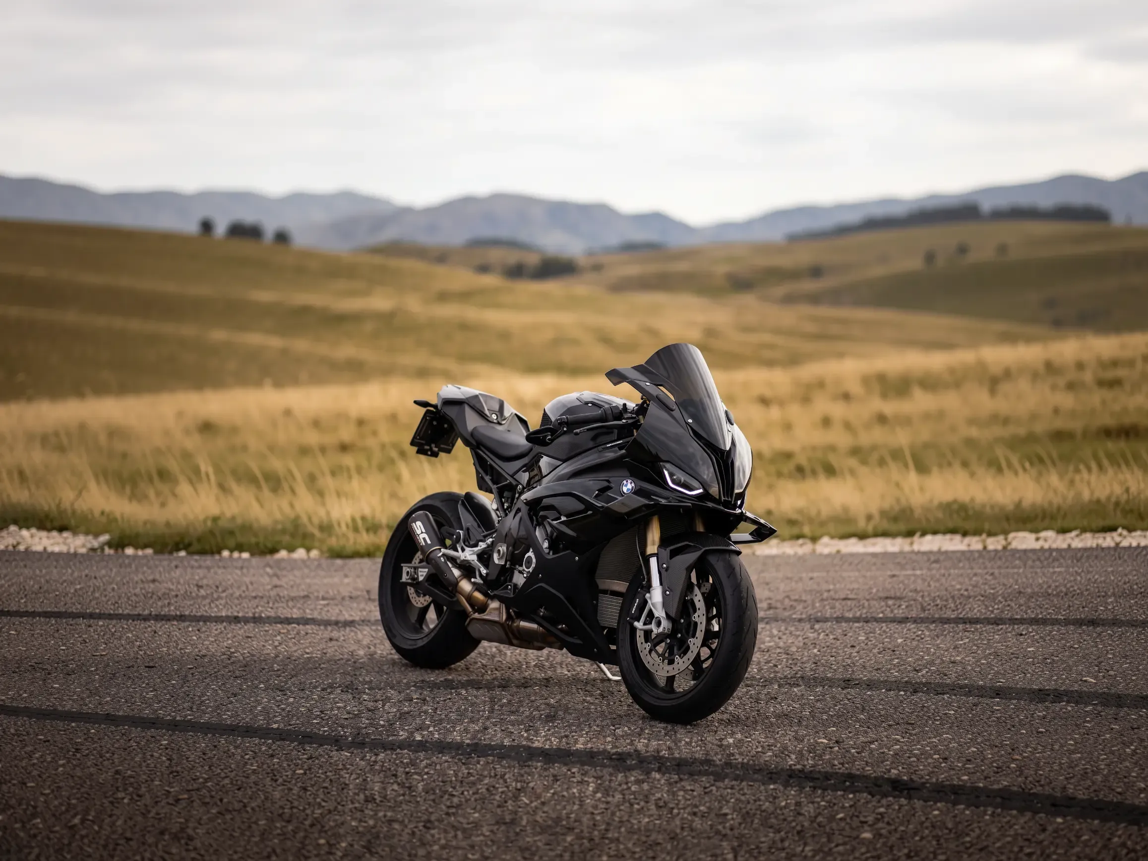 Schwarzes Superbike BMW S1000RR, geparkt auf einer Straße über sanften Hügeln.